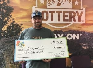 Jasper F. de Fort Morgan sosteniendo un cheque de gran tamaño por $10,000 frente al fondo de la Lotería de Colorado.