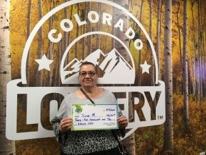 Silvia M. sosteniendo un cheque gigante de $35,000 frente al fondo de la Lotería de Colorado