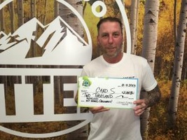 Chad S. and daughter holding an oversized check for $2,000 in front of Colorado Lottery background