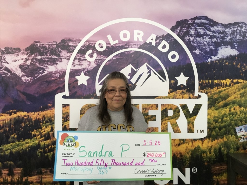 Winner holding oversized check in Colorado Lottery claims office.