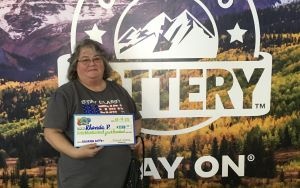 Rhonda P. sosteniendo un cheque de gran tamaño por $1,500 frente al fondo de la Lotería de Colorado