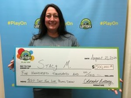 Stacy M. of Commerce City holding an oversized check for $500,000 in front of Colorado Lottery background.