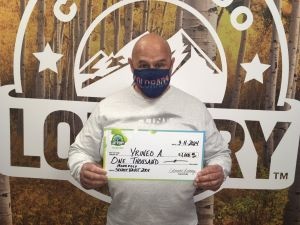 Yrineo A. sosteniendo el cheque gigante de $1,000 frente al fondo de Colorado Lottery