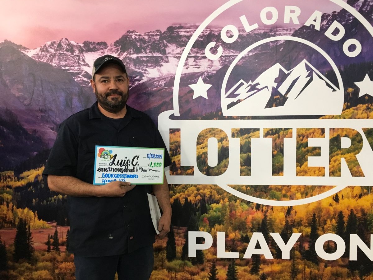 Luis C. holding an oversized check for $1,000 in front of Colorado Lottery background