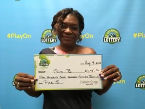 Gina B. de Denver sosteniendo un cheque de gran tamaño por $1,450 frente al fondo de la Lotería de Colorado.