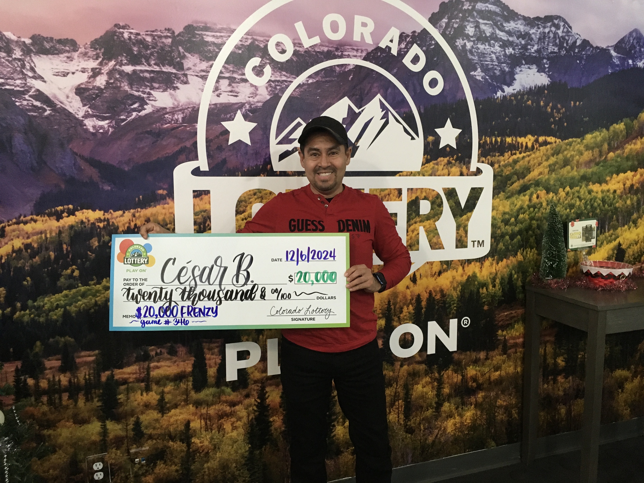 Cesar B.  sosteniendo el cheque gigante de $20,000 frente al fondo de Colorado Lottery