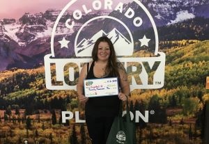 Crystal H. sosteniendo el cheque de $20,000 frente al fondo de Colorado Lottery