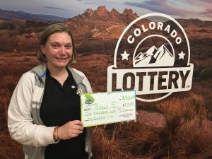 Pamela S. sosteniendo el cheque gigante de $1,000 frente al fondo de Colorado Lottery