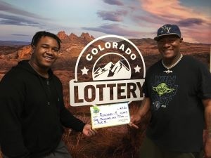 Reginald M. sosteniendo un cheque gigante de $1,000 frente al fondo de la Lotería de Colorado.