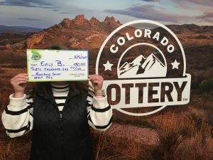Emily B. holding an oversized check for $30,000 in front of Colorado Lottery background