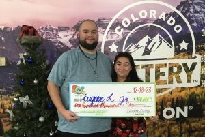 Eugene L. sosteniendo su cheque de gran tamaño por $100,000 frente al fondo de la Lotería de Colorado