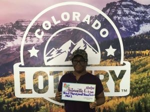 Antoinette G. sosteniendo un cheque de gran tamaño por $3.300 frente al fondo de la Lotería de Colorado