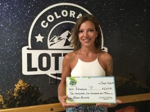 Katherine P. de Denver sosteniendo un cheque de gran tamaño por $2,500 frente al fondo de la Lotería de Colorado.