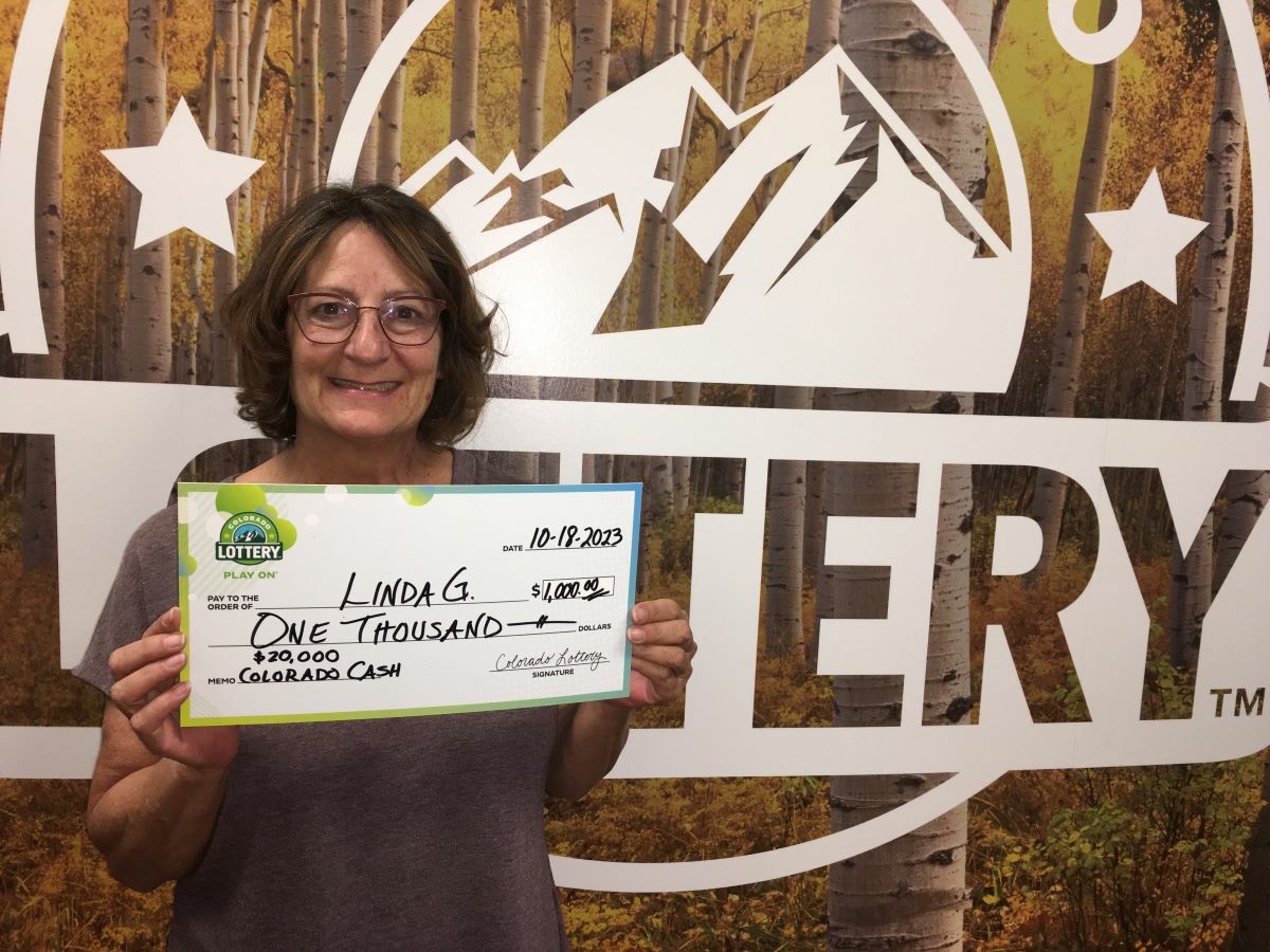 Linda G holding an oversized check for $1,000 in front of Colorado Lottery background