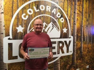 James S. sosteniendo un cheque gigante por $2,100 frente al fondo de la Lotería de Colorado