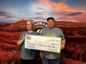 Jeffrey y April sosteniendo su cheque por $100,000 frente al fondo de la Lotería de Colorado