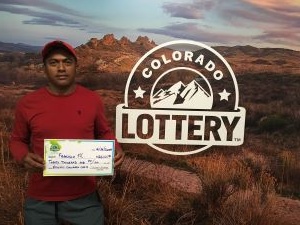 Francisco M. sosteniendo un cheque gigante de $20,000 frente al fondo de Colorado Lottery