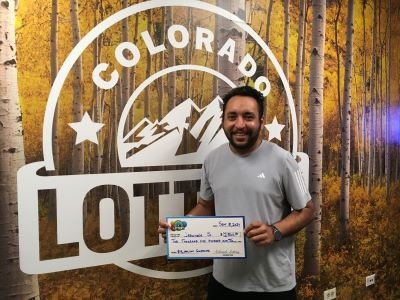 Jaswinder S. sosteniendo un cheque gigante de $2,500 frente al fondo de la Lotería de Colorado