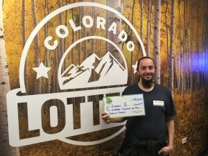 Andrew S. sosteniendo un cheque de gran tamaño por $200,000 frente al fondo de la Lotería de Colorado