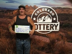 Wayne L. sosteniendo un cheque de gran tamaño por $1,000 frente al fondo de la Lotería de Colorado