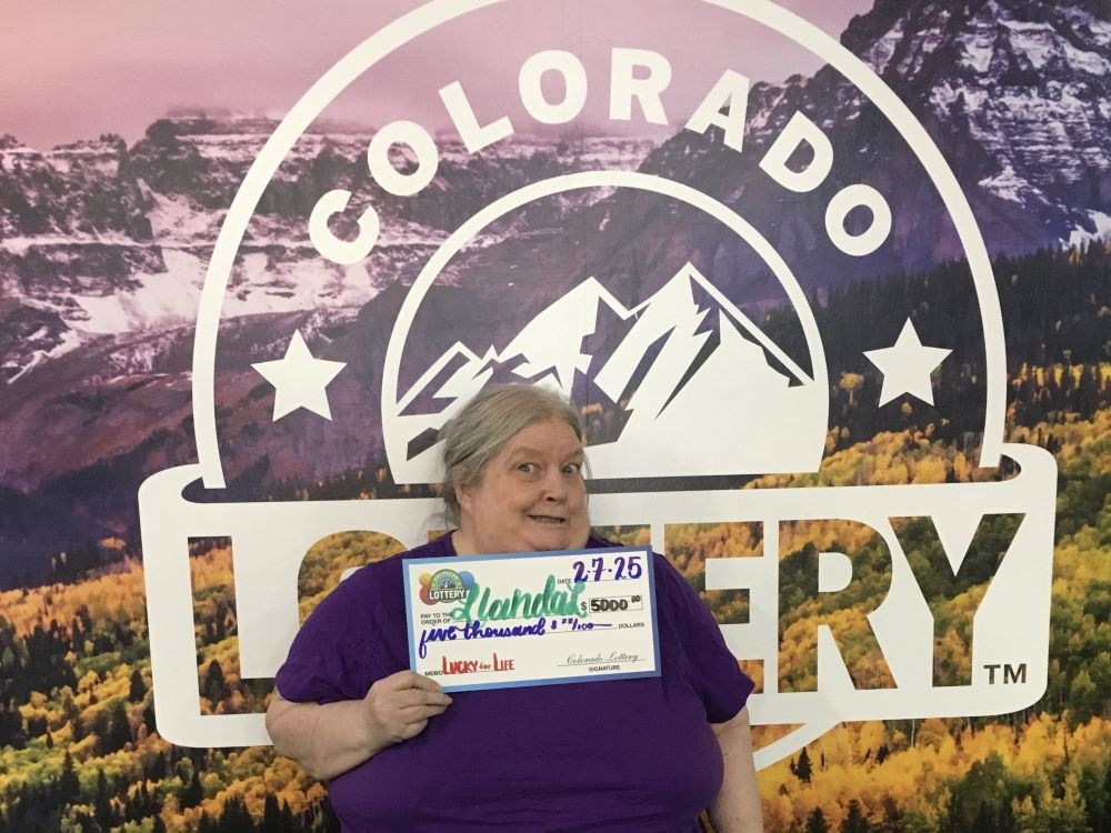 El ganador sostiene un cheque de gran tamaño frente a un fondo de la Lotería de Colorado