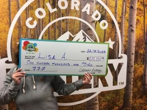 Lisa A. sosteniendo su cheque de gran tamaño por $100,000 frente al fondo de la Lotería de Colorado