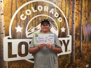 Danah J. sosteniendo un cheque de gran tamaño por $1,000 frente al fondo de la Lotería de Colorado