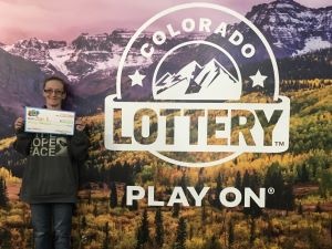 Shari K. sosteniendo el cheque gigante de $30,000 frente al fondo de Colorado Lottery