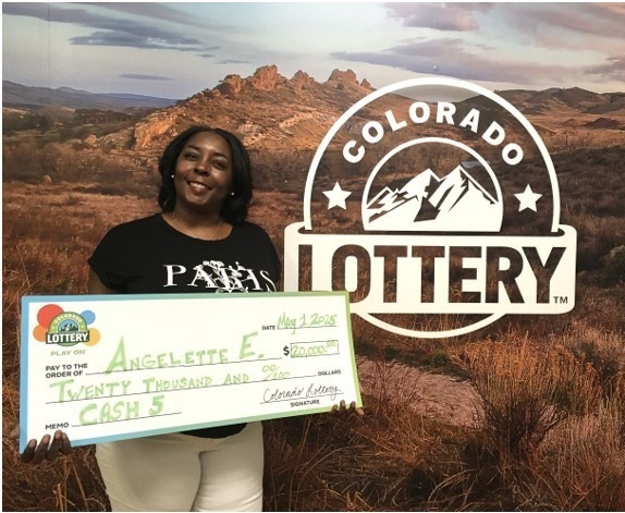Ganador sosteniendo un cheque de gran tamaño en la oficina de reclamos de la Lotería de Colorado.