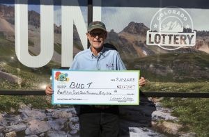 Waldemar "Bud" T. de Montrose sosteniendo un cheque de gran tamaño por $5,067,041 frente al fondo de la Lotería de Colorado.