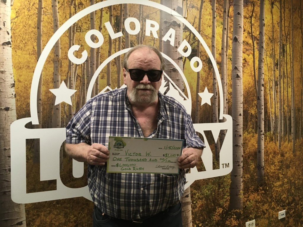 Victor W. sosteniendo un cheque por $1,000 frente a un fondo de la Lotería de Colorado.