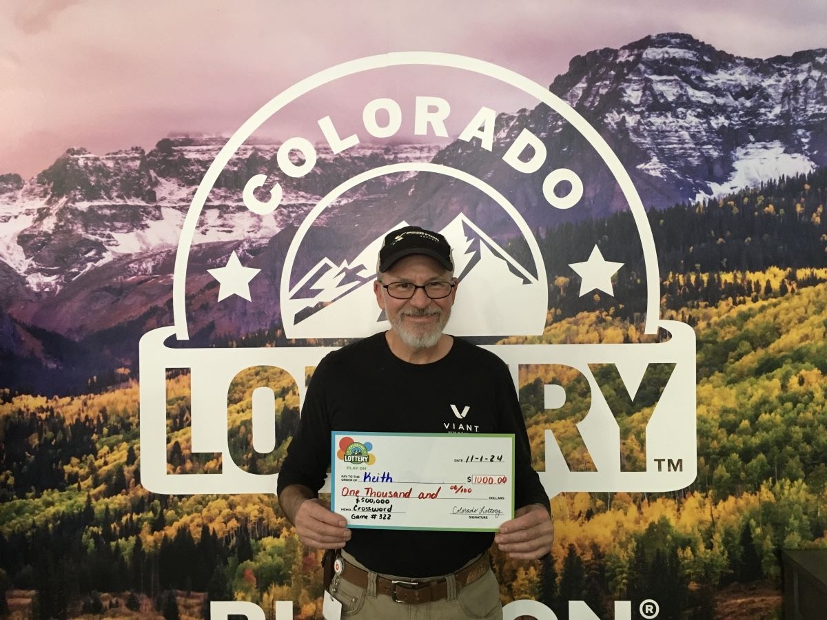 Keith C. sosteniendo el cheque gigante de $1,000 frente al fondo de Colorado Lottery