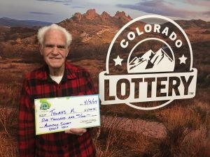 Thomas M. sosteniendo el cheque gigante de $1,000 frente al fondo de Colorado Lottery