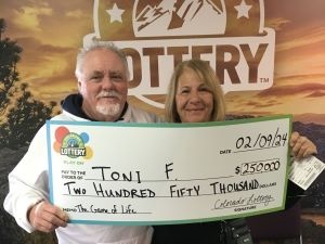 Toni F. sosteniendo un cheque de gran tamaño por $250,000 frente al fondo de la Lotería de Colorado