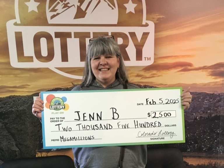 Jenn B. sosteniendo un cheque gigante frente al fondo de la Lotería de Colorado