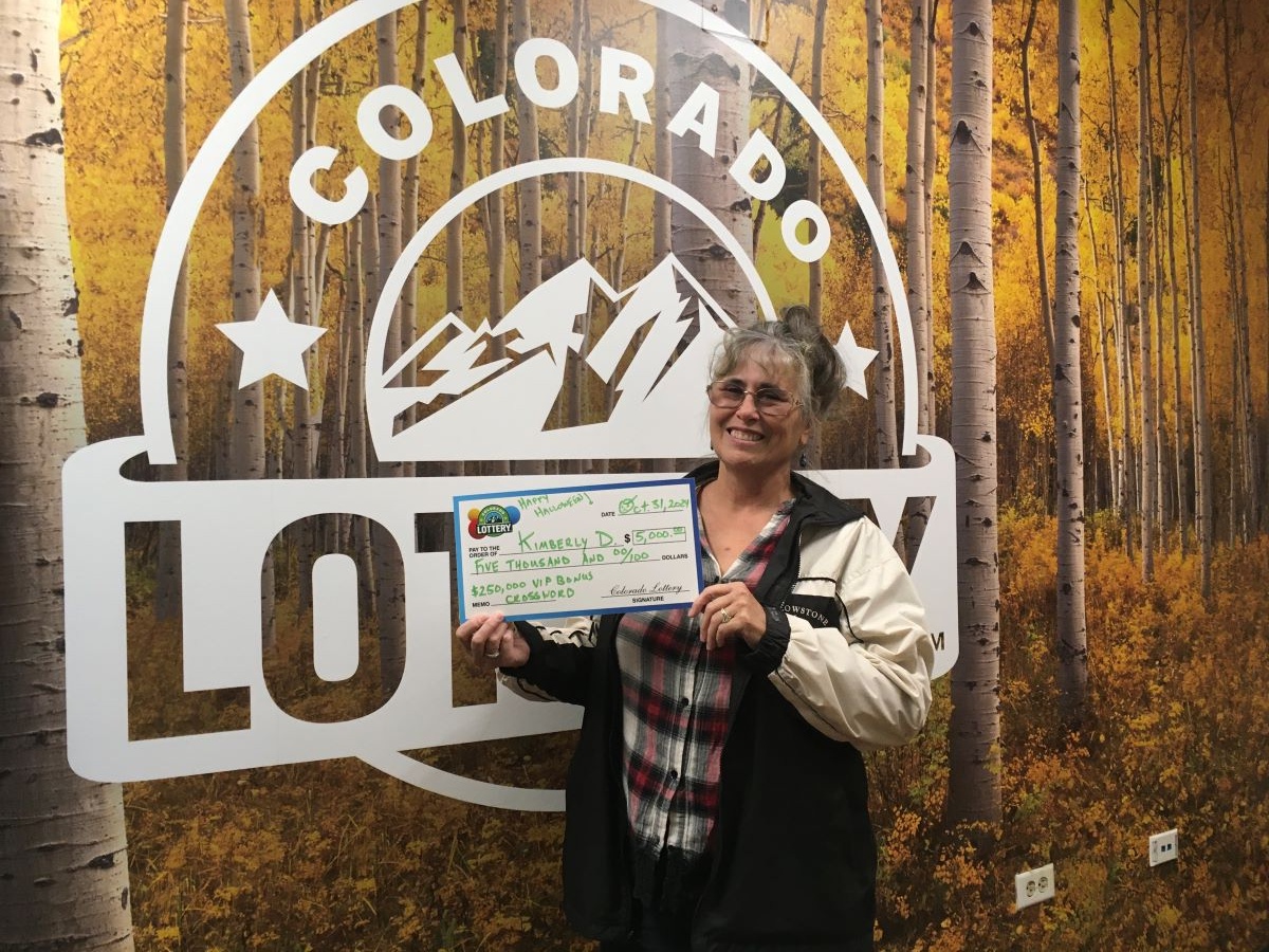 Kimberly D. sosteniendo el cheque gigante de $5,000 frente al fondo de Colorado Lottery