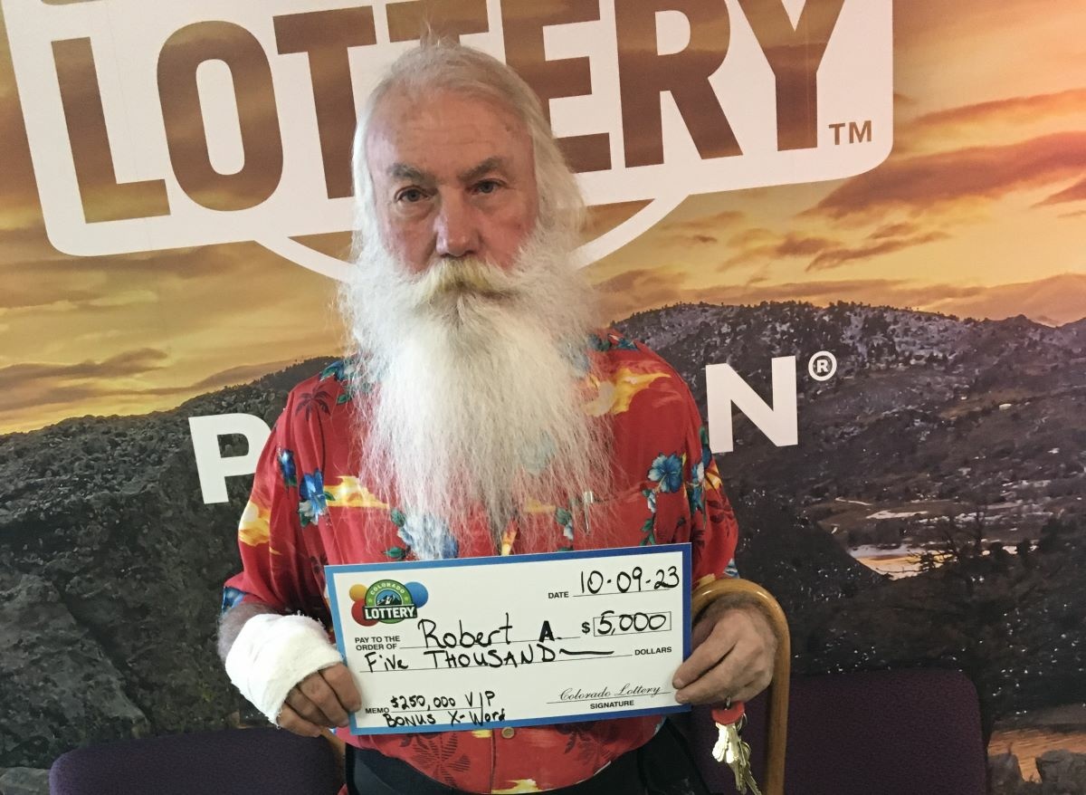 Robert A. holding an oversized check for $5,000 in front of Colorado Lottery background