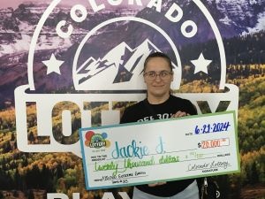 Jackie J. holding an oversized check for $20,000 in front of Colorado Lottery background