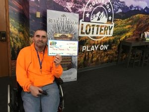 Tracy T. sosteniendo el cheque gigante de $40,000 frente al fondo de Colorado Lottery