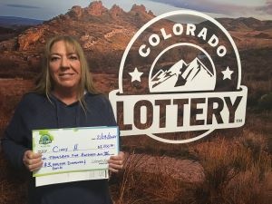 Cindy H. sosteniendo el cheque gigante de $2,500 frente al fondo de Colorado Lottery