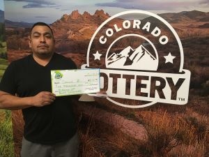 Carlos Z. holding check for $5,000 in front of Colorado Lottery background