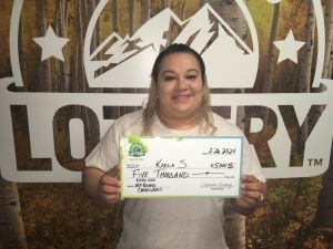 Karla S. sosteniendo el cheque gigante de $5,000 frente al fondo de Colorado Lottery