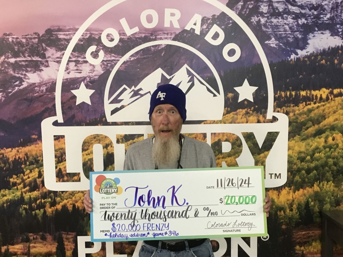 John K. holding $20,000 oversized check in front of Colorado Lottery background