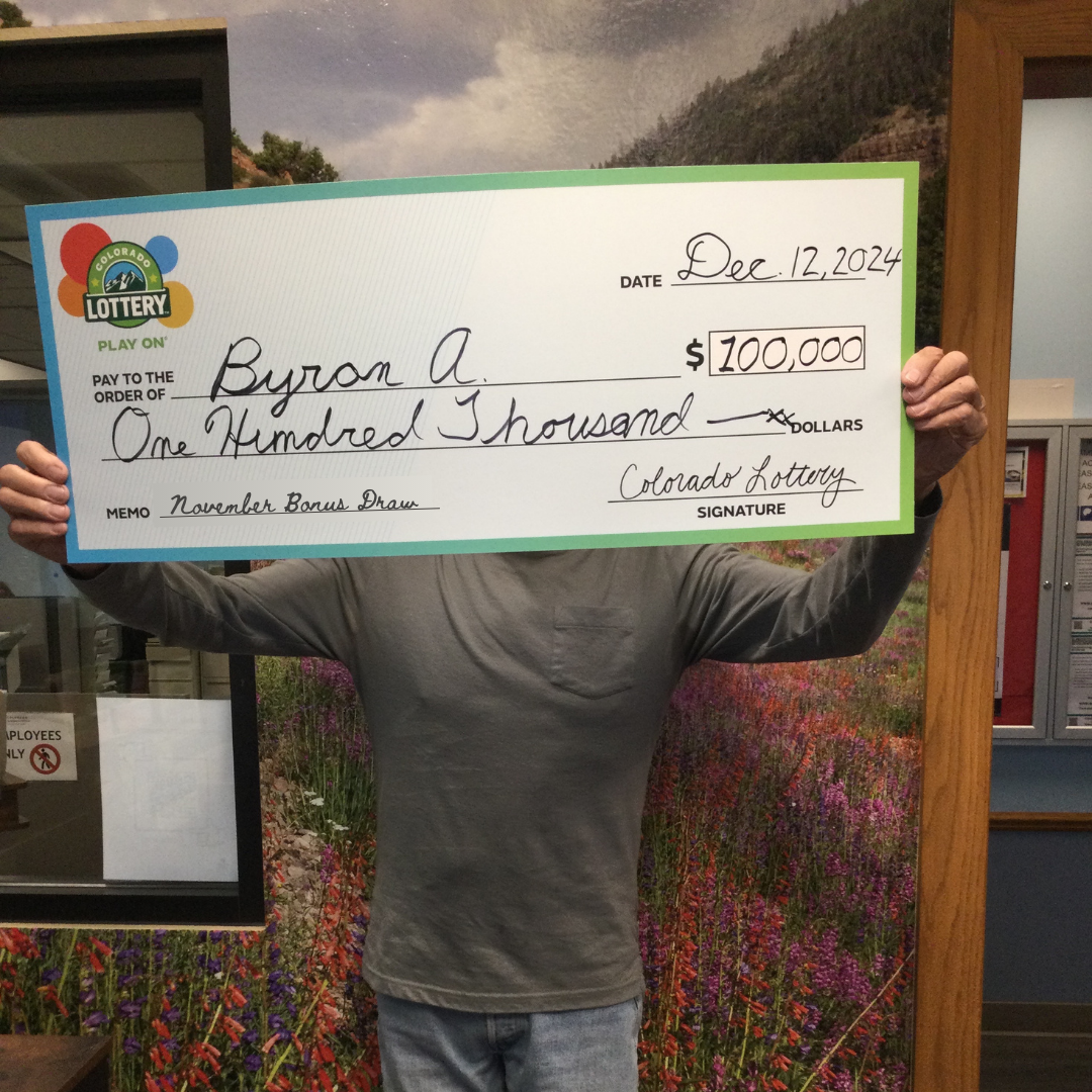 Byron A. posando con su cheque de $100,000 frente al fondo del Colorado Lottery.