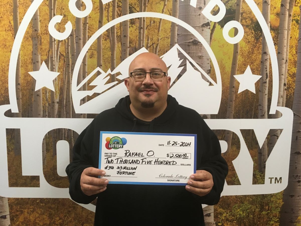 Rafael O. sosteniendo un cheque de gran tamaño de $2,500 frente a un fondo de la Lotería de Colorado