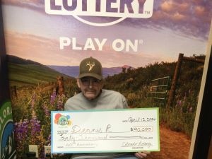 Dennis R. sosteniendo el cheque gigante de $40,000 frente al fondo de Colorado Lottery