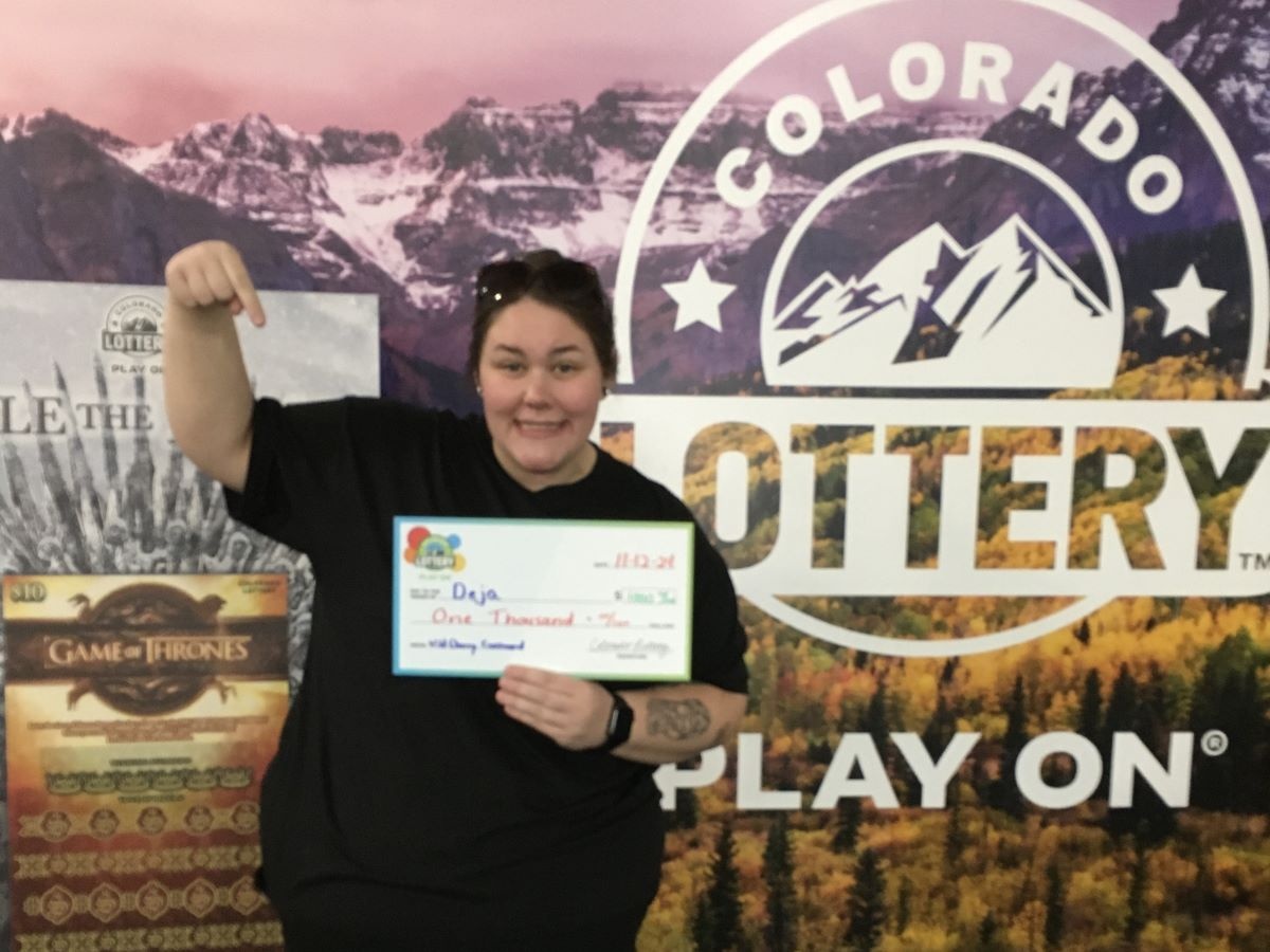 Deja B. holding an oversized check for $1,000 in front of Colorado Lottery background