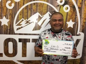 Luis G. holding an oversized check for $5,000 in front of Colorado Lottery background
