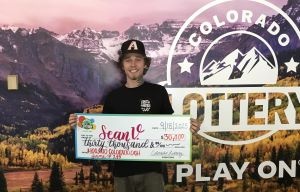 Sean V. de Colorado Springs sosteniendo un cheque de gran tamaño por $30,000 frente al fondo de la Lotería de Colorado