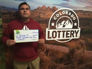 Santos C. holding an oversized check for $20,000 in front of Colorado Lottery background